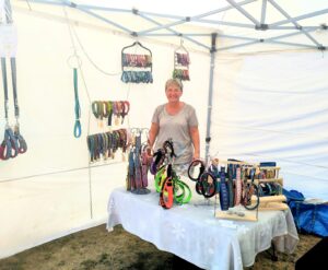 Anita am Stand der Halsbandwerkstatt im Zelt am Thurland Jumpers Cup, umgeben von aufgehängten Hundehalsbändern und Leinen